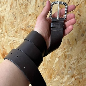 May include: A dark brown leather belt with a silver buckle. The buckle has a textured design. The word "DIESEL" is embossed on the belt near the buckle. The belt is rolled up.