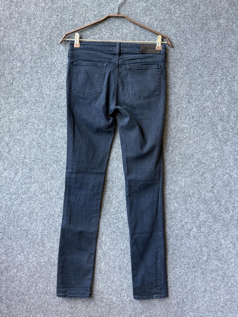 Op de afbeelding: Een donkergrijze spijkerbroek hangend aan een bruine kledinghanger. De broek heeft twee achterzakken, een tailleband met riemlussen en een rechthoekig leren merklabel aan de achterkant rechts op de tailleband. De denim heeft een slim fit model.
