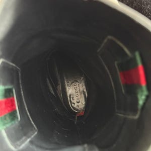 Op de afbeelding: Zwarte leren Gucci-laars met het Gucci-logo zichtbaar op de binnenzool. De laars heeft een groen en rood streepdetail aan de zijkant. De binnenkant van de laars is zwart.