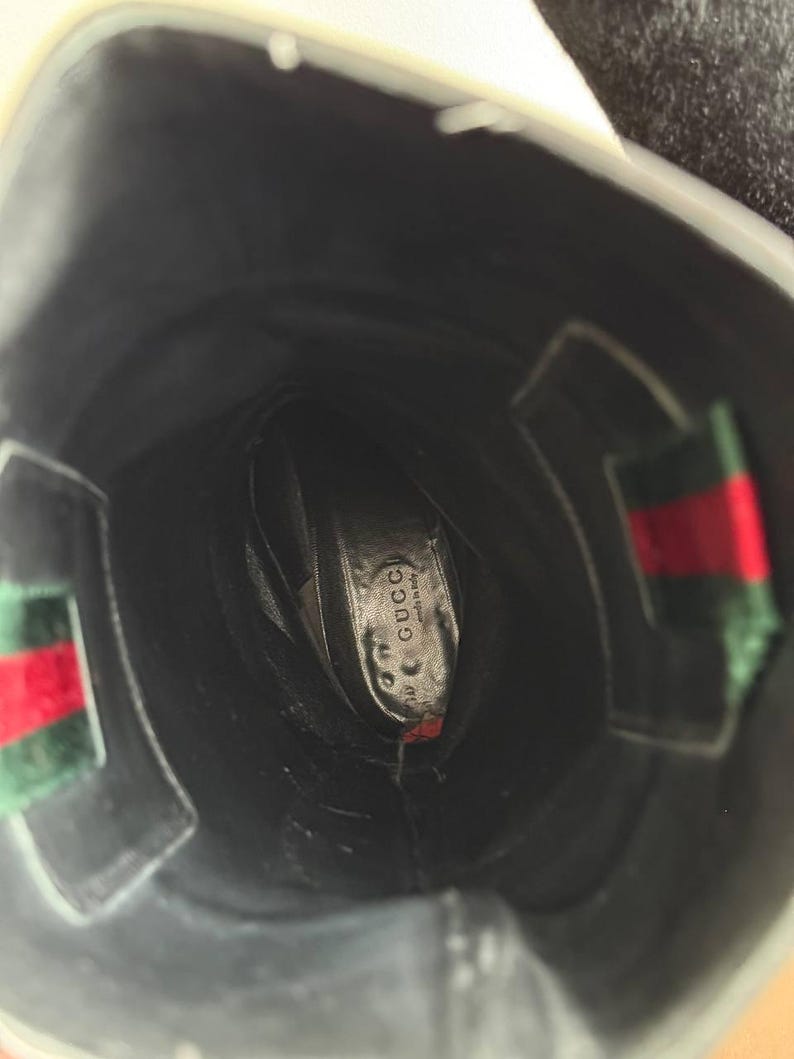 Op de afbeelding: Zwarte leren Gucci-laars met het Gucci-logo zichtbaar op de binnenzool. De laars heeft een groen en rood streepdetail aan de zijkant. De binnenkant van de laars is zwart.