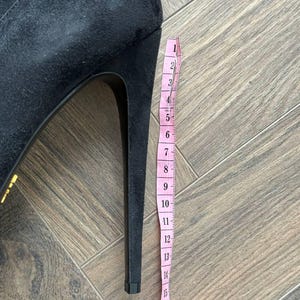 May include: Black suede high-heeled boot with a stiletto heel. A pink measuring tape is placed next to the heel, showing a height of approximately 7 inches.