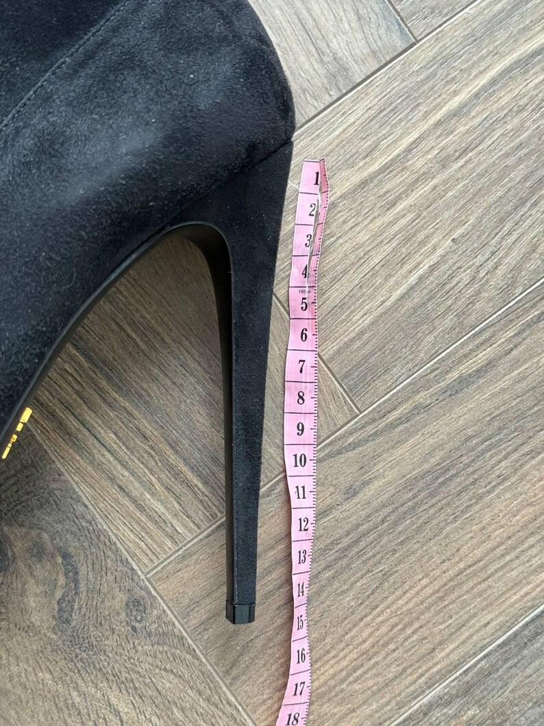 May include: Black suede high-heeled boot with a stiletto heel. A pink measuring tape is placed next to the heel, showing a height of approximately 7 inches.