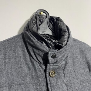 May include: A gray wool jacket with a black quilted lining. The jacket has a button closure and a stand-up collar.
