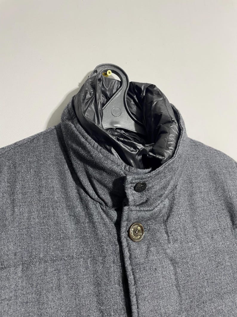 May include: A gray wool jacket with a black quilted lining. The jacket has a button closure and a stand-up collar.
