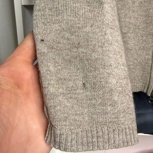 Pu&ograve; includere: Primo piano di una manica di maglione marrone chiaro. La manica &egrave; realizzata in materiale a maglia con polsino a coste. Ci sono piccole imperfezioni nel tessuto a maglia. Il maglione sembra essere di un colore neutro.