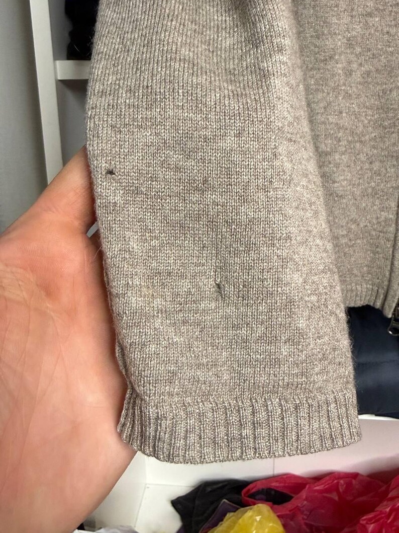 Pu&ograve; includere: Primo piano di una manica di maglione marrone chiaro. La manica &egrave; realizzata in materiale a maglia con polsino a coste. Ci sono piccole imperfezioni nel tessuto a maglia. Il maglione sembra essere di un colore neutro.