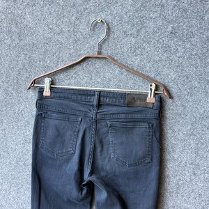 Op de afbeelding: Een donkergrijze spijkerbroek van denim met twee achterzakken, een tailleband met riemlussen en een rechthoekige leren patch aan de rechterachterkant met de merknaam Acne Studios in een subtiel, donker lettertype gedrukt.