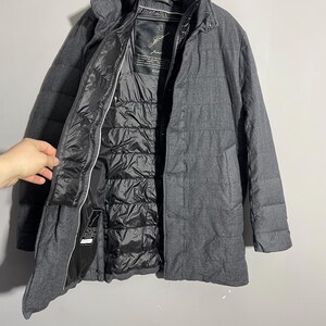 May include: A gray wool coat with a black quilted lining. The coat has a zipper closure and two pockets. The label on the inside of the coat reads "Just", with a handwritten signature.