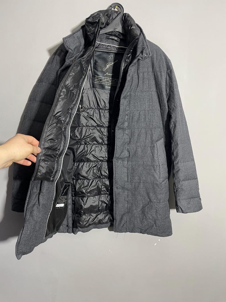 May include: A gray wool coat with a black quilted lining. The coat has a zipper closure and two pockets. The label on the inside of the coat reads "Just", with a handwritten signature.
