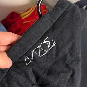 Pode incluir: T-shirt preto com texto bordado em branco. O texto diz "AKROS Fantomas Special 2008". A t-shirt est&aacute; pendurada num cabide preto. Outras pe&ccedil;as de roupa s&atilde;o vis&iacute;veis no fundo.