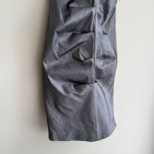 Puede incluir: Un vestido gris sin tirantes con un dise&ntilde;o fruncido. El vestido est&aacute; hecho de una tela brillante y texturizada y cuelga verticalmente contra una pared blanca. El vestido parece ser hasta la rodilla.