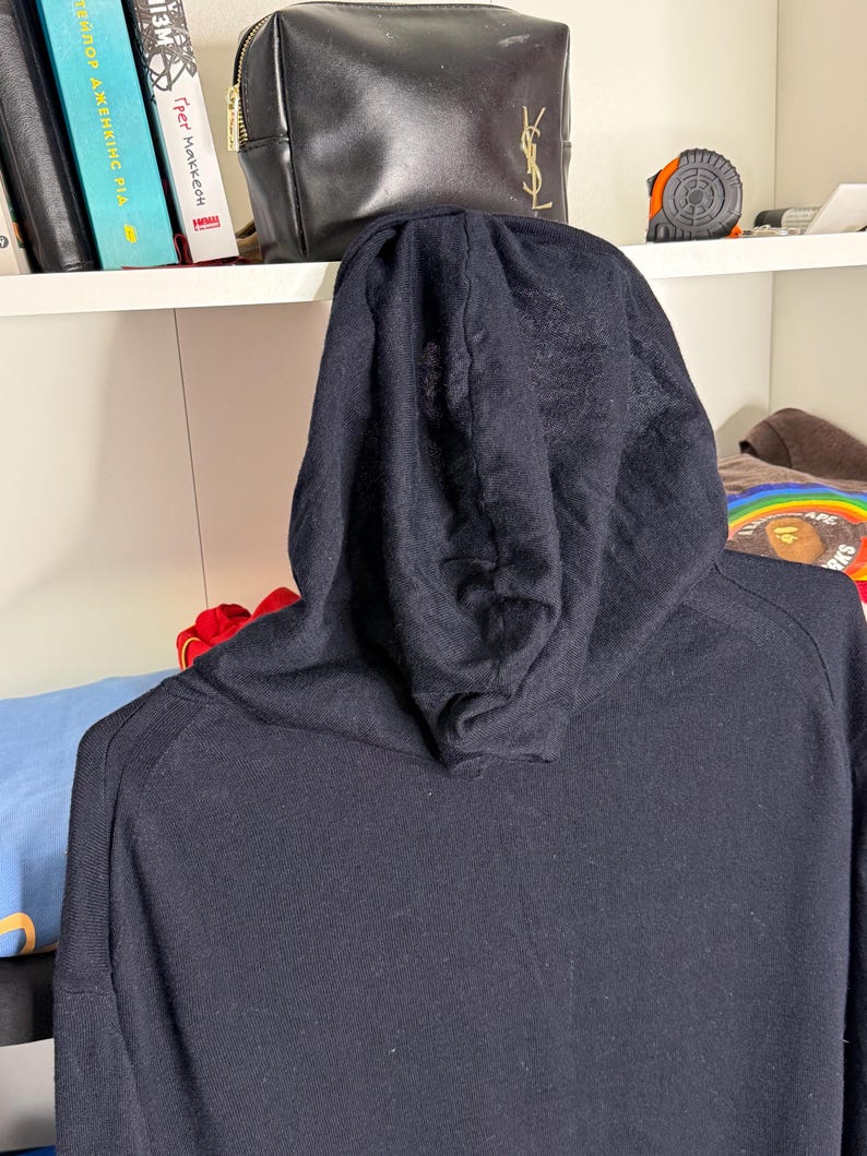 May include: A black hooded sweatshirt with a drawstring hood. The sweatshirt is made of a soft, knit fabric. The image is taken from the back, showing the hood and the top of the shoulders.