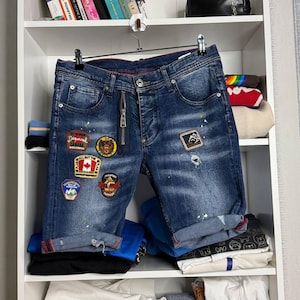 May include: Blue denim shorts with multiple patches and a zipper fly. The shorts have a distressed look with a few small holes and rolled-up cuffs. The patches feature various designs and text.