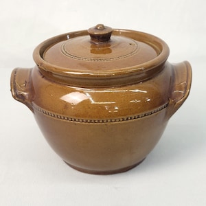 May include: A brown ceramic pot with a lid and two handles. The pot has a beaded design around the rim.