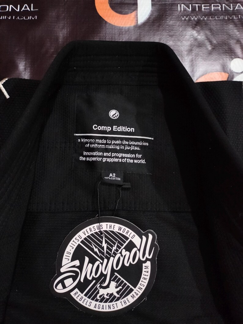 May include: Black jiu-jitsu gi with a tag that reads "Shoyoroll" and "Comp Edition." The gi has a collar and is made of cotton. The tag also states "Jiu-Jitsu Versus The World."