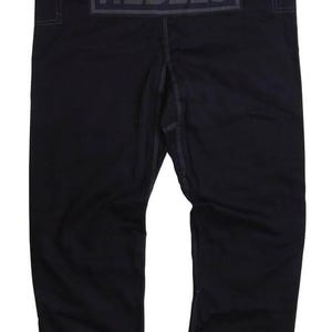 Op de afbeelding: Zwarte vechtsportbroek met het woord "REBELS" in donkergrijze letters op de rug. De broek heeft witte stiksels en een relaxte pasvorm. De broek is gemaakt van een duurzaam materiaal.