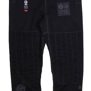 Op de afbeelding: Zwarte Jiu-Jitsu broek met versterkte stiksels en patches. De broek heeft het "Shoyoroll Jiu Jitsu" logo en andere merkemblemen. Het ontwerp bevat grijze accenten en een getailleerde pasvorm, geschikt voor vechtsporttraining.