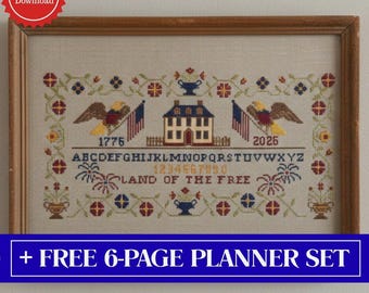 May include: A framed cross-stitch sampler with patriotic imagery. The design includes a house, eagles, flags, and the text "1776" and "2025". The words "LAND OF THE FREE" and the alphabet are also included. The frame is made of wood.