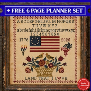 May include: Framed cross-stitch sampler with an American flag, birds, and floral basket. The sampler includes the text "LAND THAT I LOVE", the years 1776 and 2026, and the alphabet. The frame is dark brown.