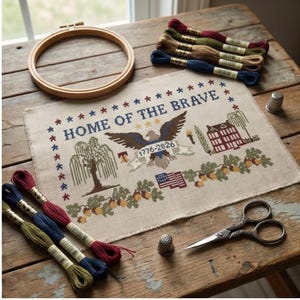 May include: A cross-stitch project with the text "HOME OF THE BRAVE" and an eagle design, surrounded by stars. The image includes embroidery floss, a wooden hoop, scissors, and thimbles, all arranged on a rustic wooden surface.