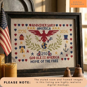 May include: Framed cross-stitch artwork with a patriotic theme. The design features a red eagle, stars, and the text "ANNIVERSARY AMERICA 1776-2026" and "GOD BLESS AMERICA HOME OF THE FREE." The frame is dark wood.
