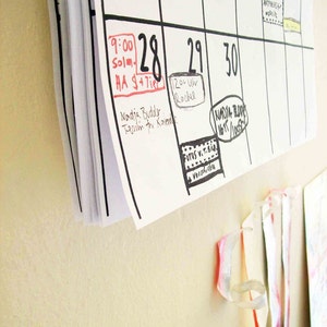 May include: A white calendar with black grid lines and handwritten appointments. The dates 28, 29, and 30 are circled in black marker. The date 28 has a red rectangle around it with the text "9:00 Solm. HA $+Tire" written inside. The date 29 has a circle around it with the text "12:00 Uhr Rachel" written inside. The date 30 has a circle around it with the text "NADJA BODE 16/1/1005" written inside.