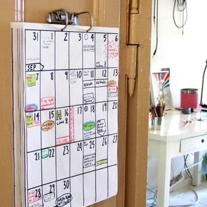 May include: A white calendar with black ink hangs on a beige door. The calendar is for September and has handwritten notes and appointments for each day.