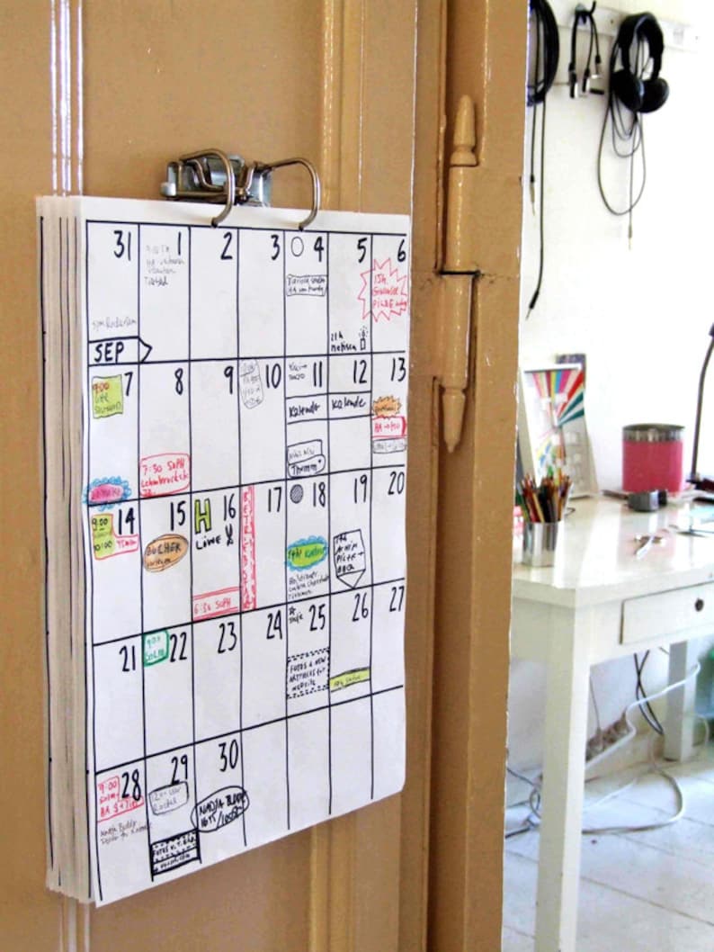 May include: A white calendar with black ink hangs on a beige door. The calendar is for September and has handwritten notes and appointments for each day.
