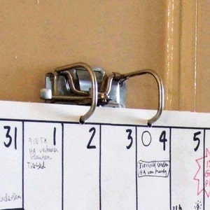 Puede incluir: Un calendario blanco con un clip de encuadernación de metal. El calendario muestra las fechas 31, 1, 2, 3, 4, 5 y 6. Hay notas escritas a mano en el calendario, incluyendo "9:00 SX", "HA verban", "Tierbed", "5pm Radetsam", "Tierbyuld senden HA von Monty" y "15th Grainless PILZE ingy".