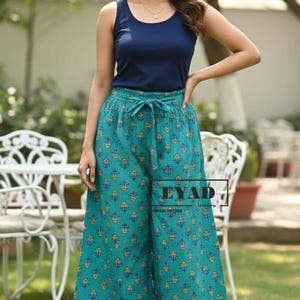 Può includere: Una donna indossa una canotta blu navy e pantaloni palazzo turchese con un motivo floreale. I pantaloni hanno una vita con coulisse. L'outfit è adatto per abbigliamento casual.