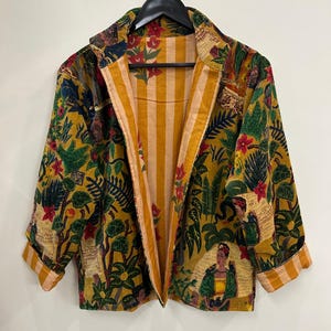 Könnte beinhalten: Eine langärmelige Jacke mit senfgelber Grundfarbe und einem lebendigen botanischen Druck aus grünem Blattwerk, roten Blumen und Porträts einer Frau mit dunklem Haar. Das Innenfutter zeigt ein vertikales gelb-weißes Streifenmuster.