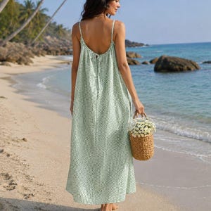 May include: A floor-length, sleeveless dress in a light green colour with a small white polka dot pattern. The dress features thin spaghetti straps, a low-cut back with a tie closure, and a loose, flowing silhouette that reaches the ankles.