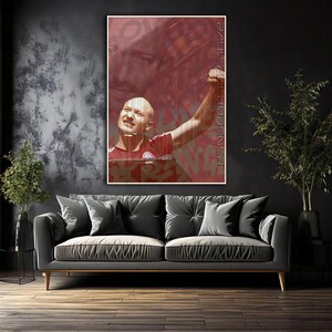 Puede incluir: Una impresión artística enmarcada que muestra a un hombre con una camiseta roja y blanca con el brazo levantado en celebración. El fondo es una mezcla de tonos rojos y marrones con texto estilo grafiti y un rostro desvanecido.