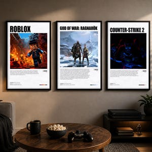Op de afbeelding: Drie ingelijste posters met de titels "ROBLOX", "GOD OF WAR: RAGNARÖK" en "COUNTER-STRIKE 2". Elke poster heeft een zwart frame en een witte achtergrond met game-afbeeldingen en tekst. De posters worden boven een bank en salontafel weergegeven.