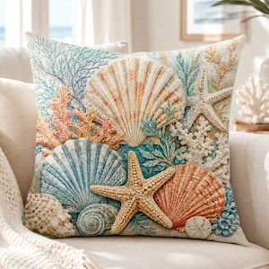 May include: A square throw pillow featuring a detailed coastal print of various seashells, including scallops and conch shells, alongside starfish, coral branches, and sea urchins in shades of blue, orange, beige, and white on a textured fabric.