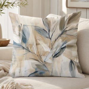 May include: A square throw pillow featuring an abstract painterly design of elongated leaves in shades of muted blue, soft gray, and warm beige. The artwork displays fluid brushstrokes and layered botanical shapes across the entire surface.
