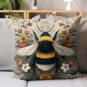 May include: Decorative square pillow featuring a large, detailed illustration of a bumblebee. The bee is depicted with yellow and black stripes, surrounded by a floral pattern with roses, daisies, and other flowers in shades of pink, yellow, and white.