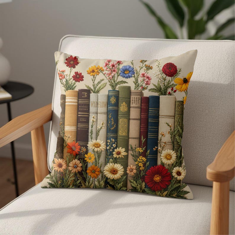May include: A square throw pillow featuring a printed design of a row of upright books in various colors including tan, brown, blue, and green. The books are interspersed and surrounded by colorful illustrations of wildflowers like daisies.