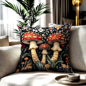 May include: Square throw pillow featuring a whimsical mushroom design. The pillow showcases large red and white spotted mushrooms against a dark blue floral background. The pillow is placed on a neutral-toned sofa.