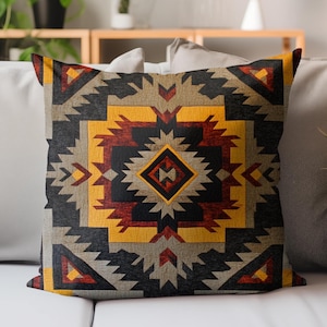 May include: Square throw pillow with a geometric pattern in shades of black, gray, yellow, and red. The design features a central diamond shape surrounded by angular shapes, creating a Southwestern or tribal aesthetic.