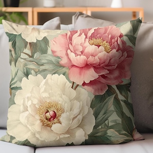 May include: Square throw pillow featuring a watercolor floral design. The pillow showcases a large pink peony and a white peony, set against a backdrop of green leaves. The flowers have yellow centers.