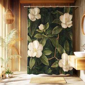 Puede incluir: Una cortina de ducha con un diseño botánico. Presenta grandes flores de magnolia blancas y hojas verdes sobre un fondo oscuro. El patrón floral crea una estética natural y elegante para el baño.