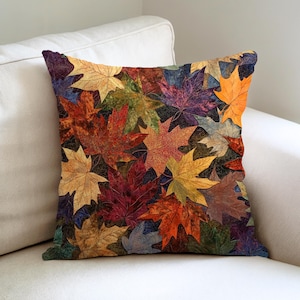 May include: Square throw pillow featuring a collage of colorful autumn leaves in shades of red, orange, yellow, and purple. The leaves are arranged in a dense pattern, creating a warm and inviting aesthetic. The pillow is placed on a white sofa.