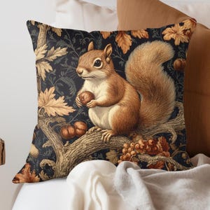 May include: Square throw pillow featuring a detailed illustration of a squirrel holding a nut, perched on a tree branch. The background is a dark blue floral pattern with autumn leaves and berries. The squirrel is brown with a fluffy tail.