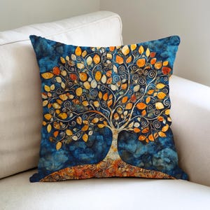 Puede incluir: Cojín cuadrado con un diseño de árbol de la vida. El cojín presenta un fondo azul con efecto acuarela. El árbol tiene un tronco y ramas blancas con hojas naranjas y amarillas. El cojín está sobre un sofá blanco.