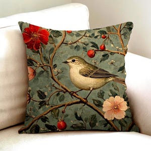 Könnte beinhalten: Ein quadratisches Zierkissen mit einem Druckmotiv eines kleinen Vogels auf einem Ast. Der Hintergrund ist in einem gedämpften Blaugrün gehalten und mit Illustrationen von roten Beeren, grünen Blättern sowie großen roten und blassrosa Blüten versehen.