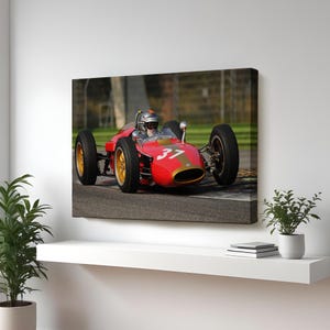May include: A red vintage race car with the number 37 on the side, driven by a racer wearing a helmet and goggles, on a race track.