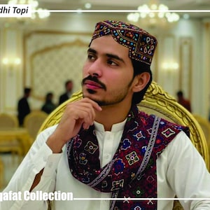 Peut inclure: Un homme portant un Sindhi Topi, un chapeau traditionnel, et une écharpe à motifs. Le chapeau est orné de broderies complexes de différentes couleurs. L'écharpe présente un motif géométrique. Le texte "Sindhi Topi" et "Sagaft Collection" sont visibles.