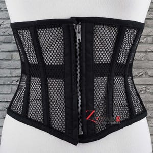 May include: Black corset featuring a mesh design with vertical panels and a front zipper closure. The corset has a structured silhouette and is designed to cinch the waist. The brand name "Z Zone Enterprises" is visible on the lower right.