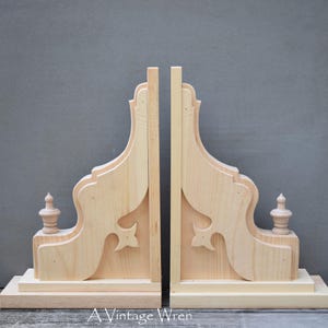 May include: Two unfinished wooden corbels with a decorative design and a finial on each side. The corbels are made of pine wood and are ready to be stained or painted.